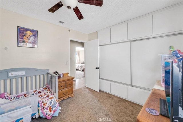 bedroom with a closet, ceiling fan, light colored carpet, and a textured ceiling