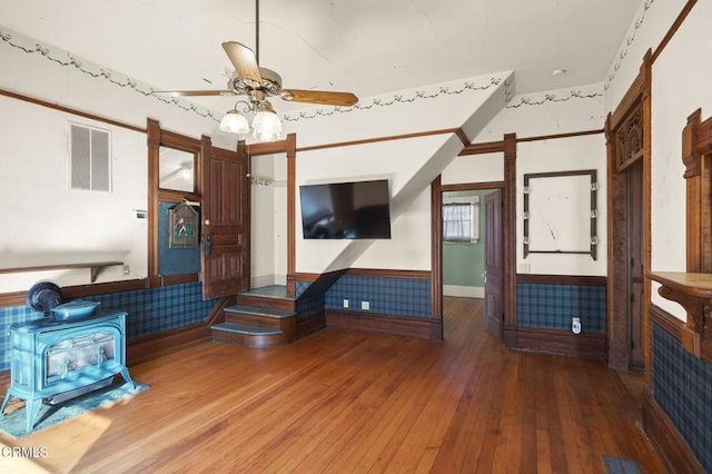 unfurnished living room featuring hardwood / wood-style floors, ceiling fan, and a wood stove