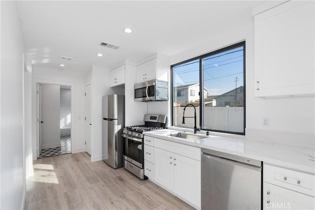 kitchen with appliances with stainless steel finishes, sink, white cabinets, and light stone counters