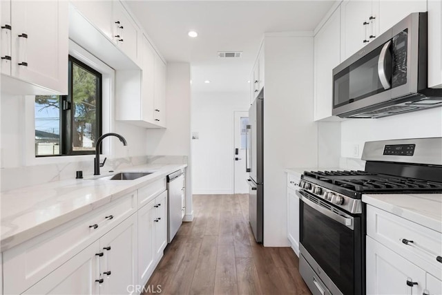 kitchen with dark wood-type flooring, sink, light stone counters, appliances with stainless steel finishes, and white cabinets