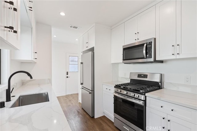 kitchen with sink, dark wood-type flooring, white cabinetry, stainless steel appliances, and light stone counters