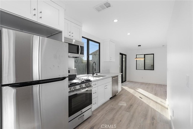 kitchen with stainless steel appliances, sink, pendant lighting, and white cabinets