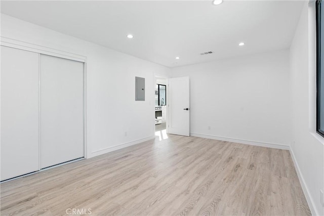 unfurnished bedroom featuring a closet, electric panel, and light hardwood / wood-style flooring