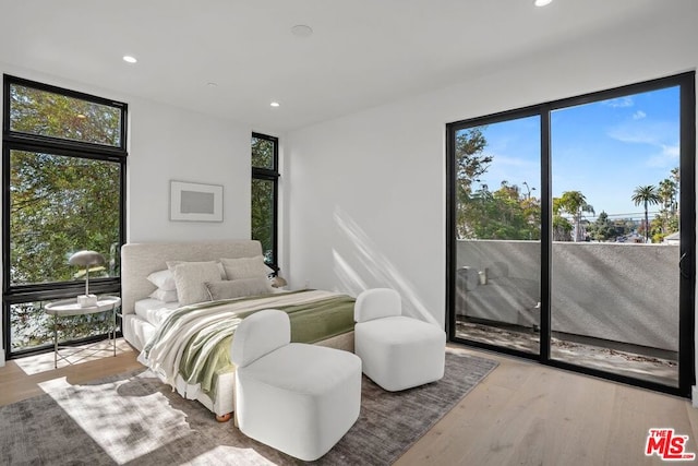 bedroom with access to exterior, light wood-type flooring, and a wall of windows