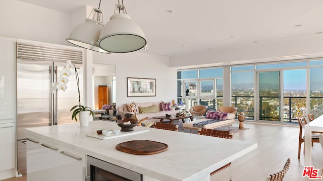 kitchen with pendant lighting, white cabinetry, stainless steel built in refrigerator, a wealth of natural light, and beverage cooler