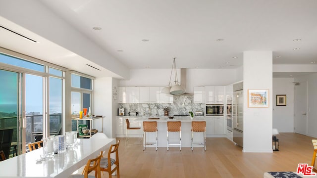 kitchen with backsplash, light hardwood / wood-style flooring, a breakfast bar, and white cabinets