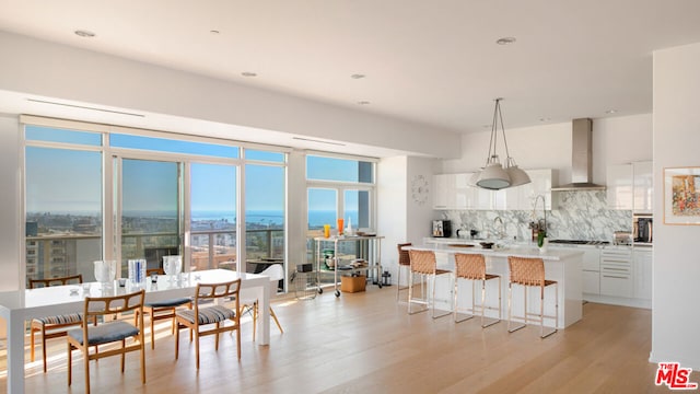 kitchen with a breakfast bar, decorative light fixtures, tasteful backsplash, white cabinetry, and wall chimney range hood