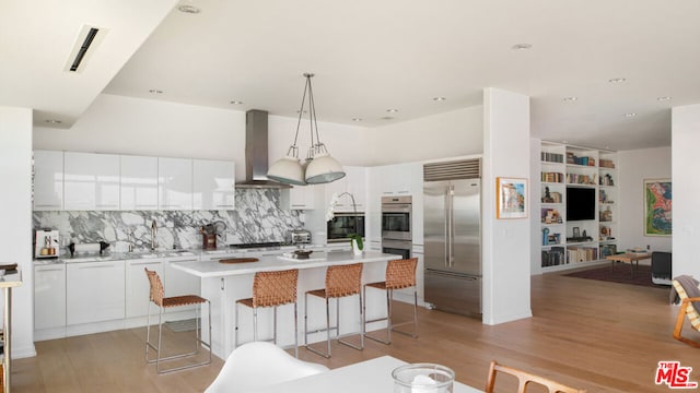 kitchen with sink, white cabinetry, island range hood, stainless steel appliances, and a kitchen island with sink