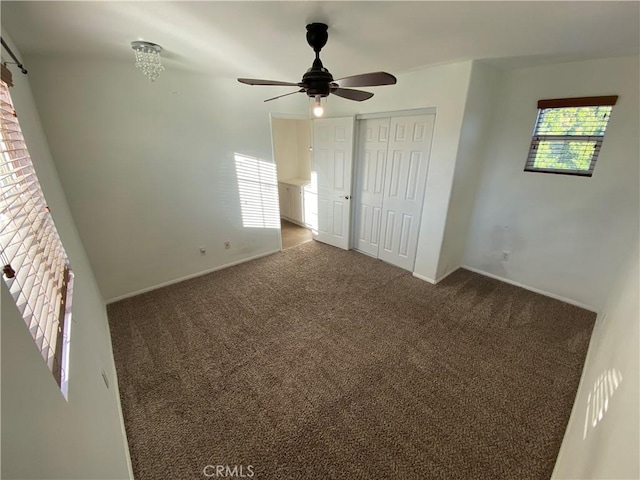 unfurnished bedroom featuring multiple windows, a closet, ceiling fan, and dark colored carpet