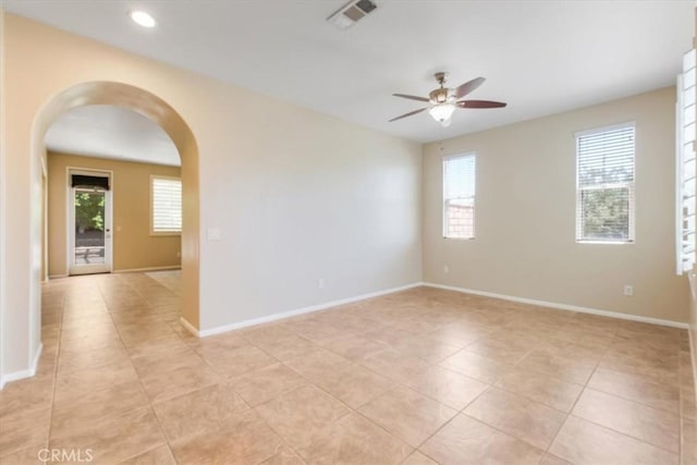 empty room with a ceiling fan, arched walkways, a healthy amount of sunlight, and visible vents