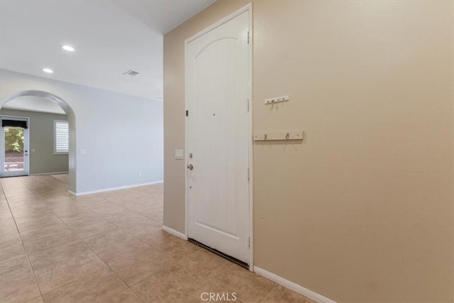 hallway featuring arched walkways, light tile patterned floors, baseboards, and recessed lighting