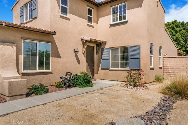 entrance to property with a patio area, a tiled roof, stucco siding, and fence