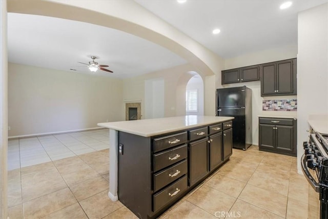 kitchen featuring range with gas cooktop, ceiling fan, arched walkways, light countertops, and freestanding refrigerator