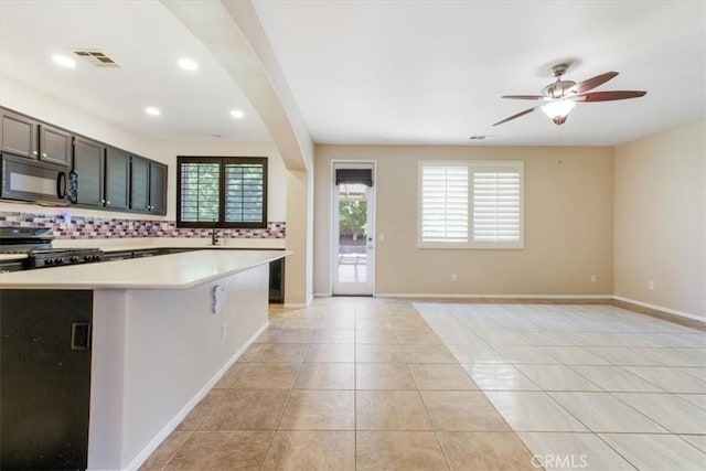 kitchen with black microwave, range, light countertops, backsplash, and visible vents