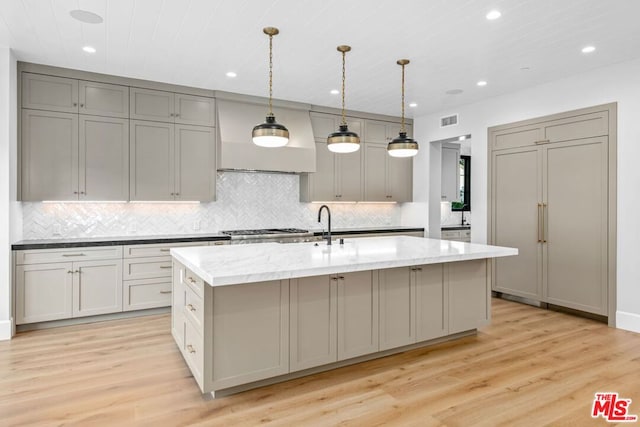 kitchen featuring hanging light fixtures, an island with sink, gray cabinetry, and light wood-type flooring