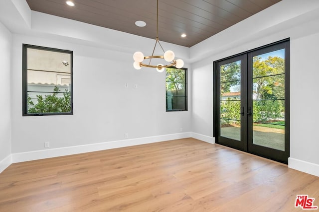 spare room featuring a raised ceiling, light hardwood / wood-style flooring, an inviting chandelier, and french doors