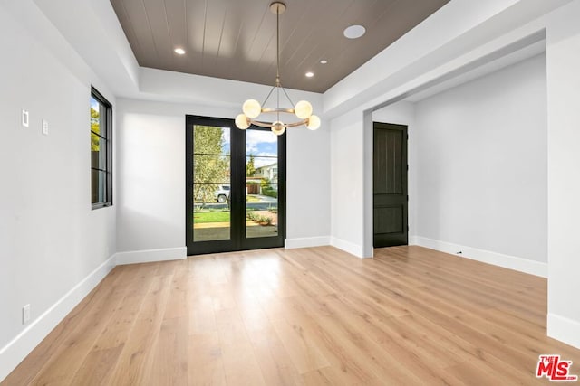 unfurnished room featuring an inviting chandelier, plenty of natural light, and light wood-type flooring