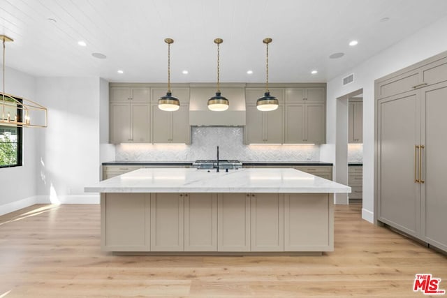 kitchen featuring a kitchen island with sink, light stone counters, gray cabinets, and light hardwood / wood-style floors