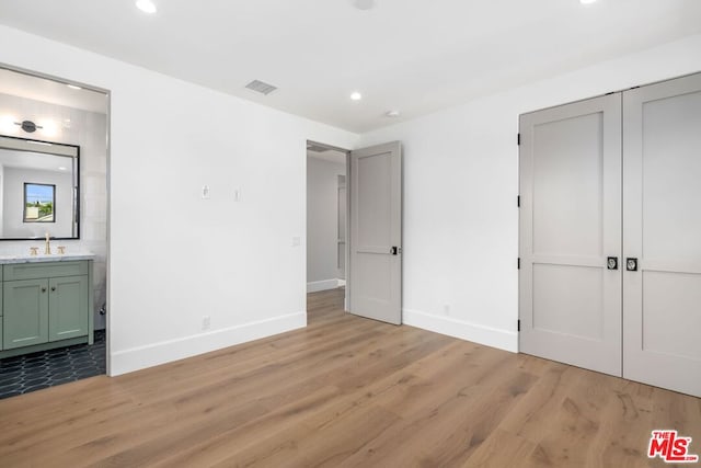 unfurnished bedroom with ensuite bath, wet bar, light hardwood / wood-style floors, and a closet