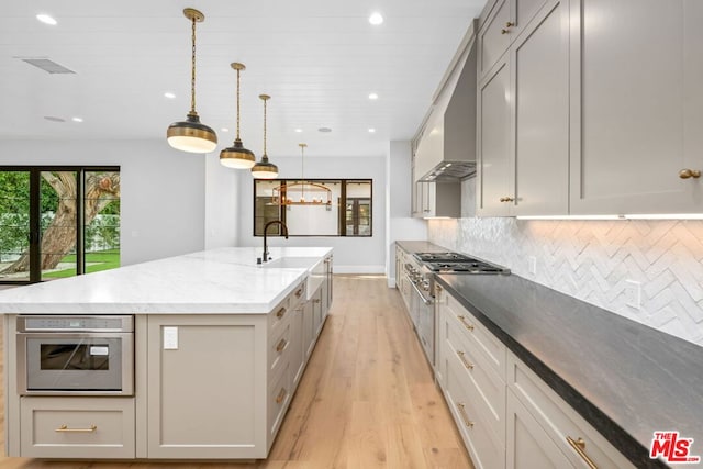 kitchen with sink, a large island, oven, decorative backsplash, and wall chimney range hood