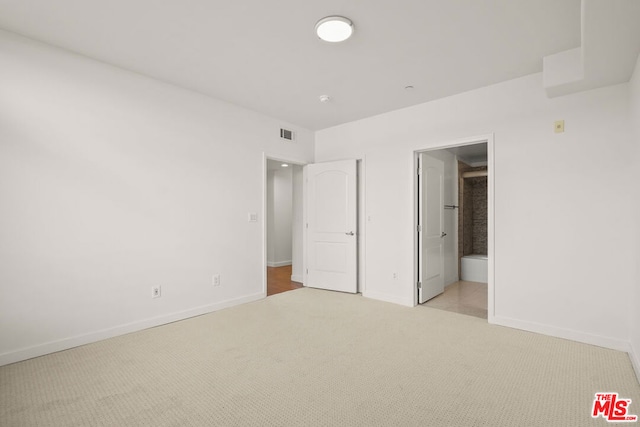 unfurnished bedroom with light carpet and connected bathroom