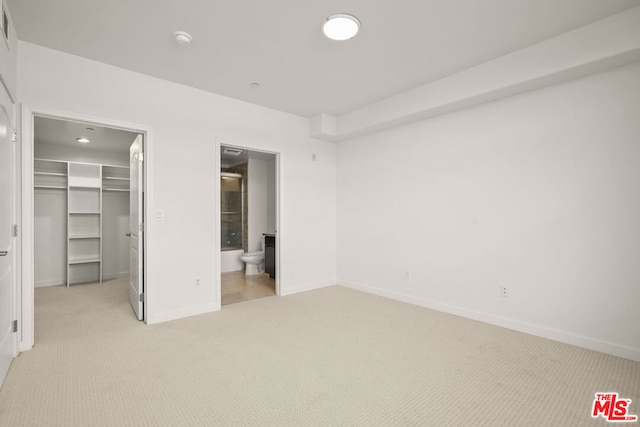 unfurnished bedroom featuring light colored carpet, a spacious closet, ensuite bath, and a closet