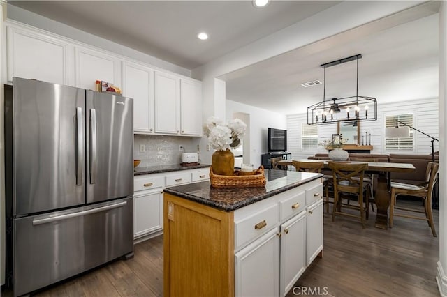 kitchen featuring a kitchen island, pendant lighting, stainless steel refrigerator, white cabinets, and dark stone counters