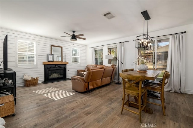 living room with ceiling fan with notable chandelier, wooden walls, hardwood / wood-style floors, and a fireplace