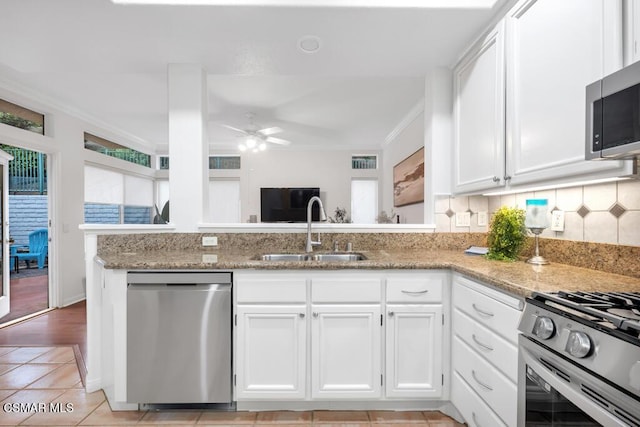 kitchen with sink, white cabinetry, stainless steel appliances, light stone countertops, and kitchen peninsula