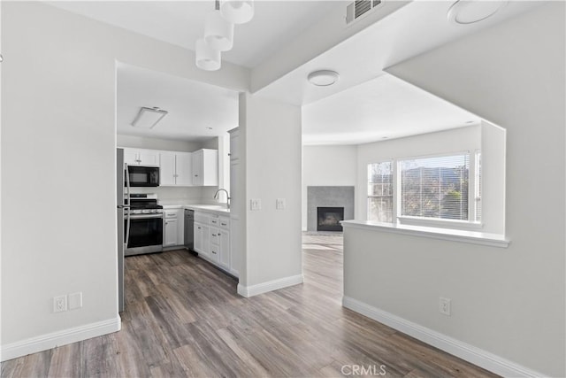 kitchen with sink, a multi sided fireplace, appliances with stainless steel finishes, hardwood / wood-style flooring, and white cabinets