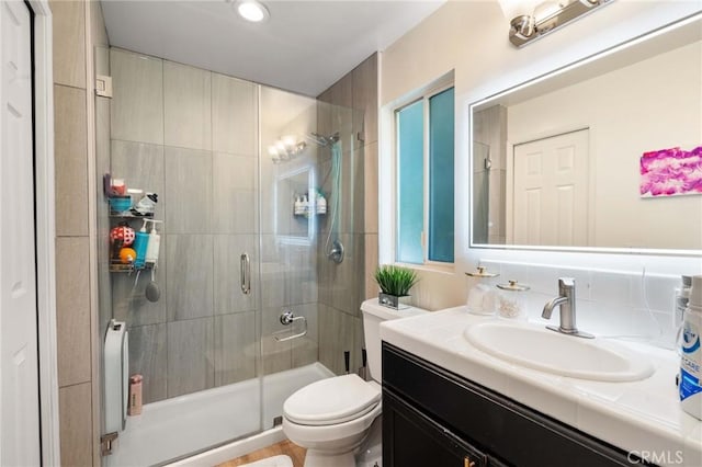 bathroom featuring a shower with door, vanity, and toilet