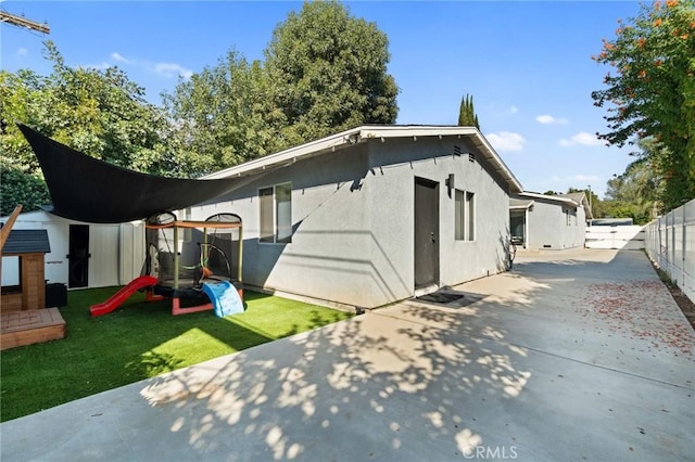 rear view of property featuring a playground and a patio area