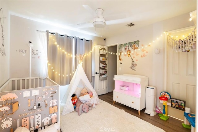 bedroom featuring dark hardwood / wood-style flooring, a nursery area, and ceiling fan