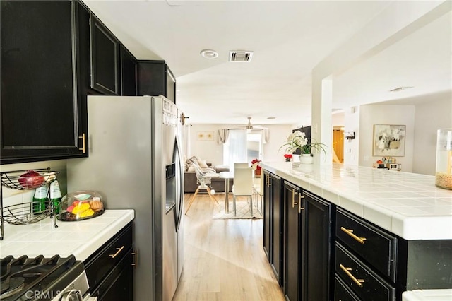 kitchen with stainless steel fridge, tile counters, light hardwood / wood-style floors, and ceiling fan