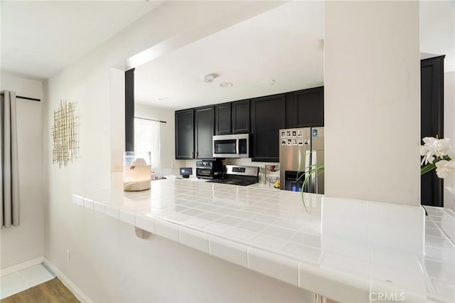 kitchen with stainless steel appliances, tile countertops, kitchen peninsula, and light hardwood / wood-style flooring