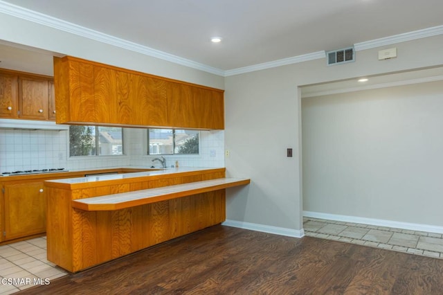 kitchen featuring tasteful backsplash, crown molding, wood-type flooring, and kitchen peninsula