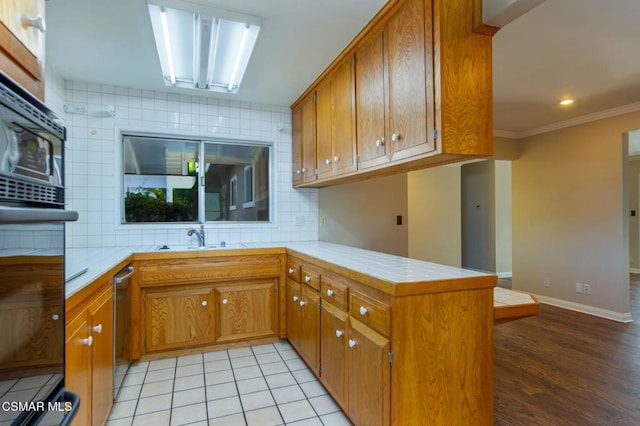 kitchen featuring crown molding, light tile patterned floors, kitchen peninsula, dishwasher, and decorative backsplash