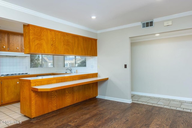 kitchen with hardwood / wood-style floors, backsplash, ornamental molding, and kitchen peninsula