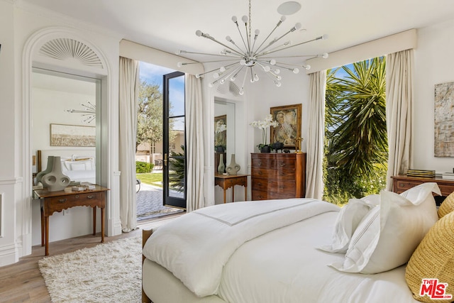 bedroom featuring multiple windows, a chandelier, light hardwood / wood-style flooring, and access to outside