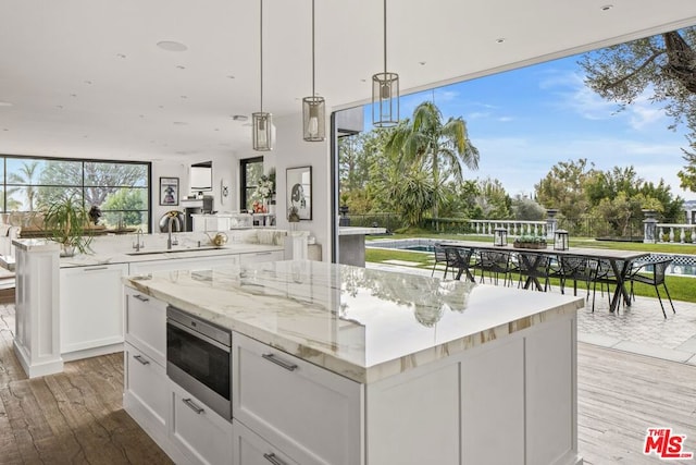 kitchen featuring sink, light stone counters, decorative light fixtures, light hardwood / wood-style floors, and white cabinets