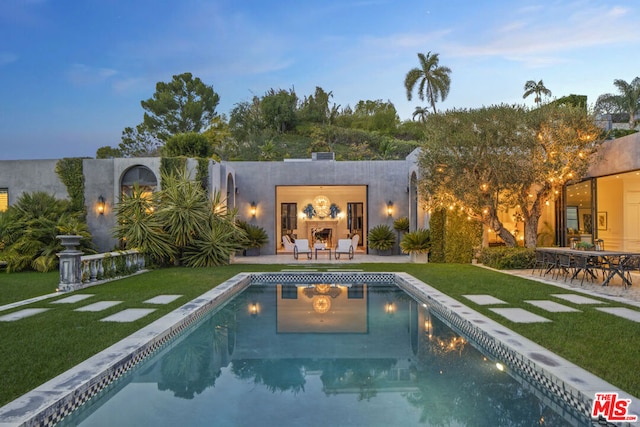 pool at dusk featuring a yard and a patio