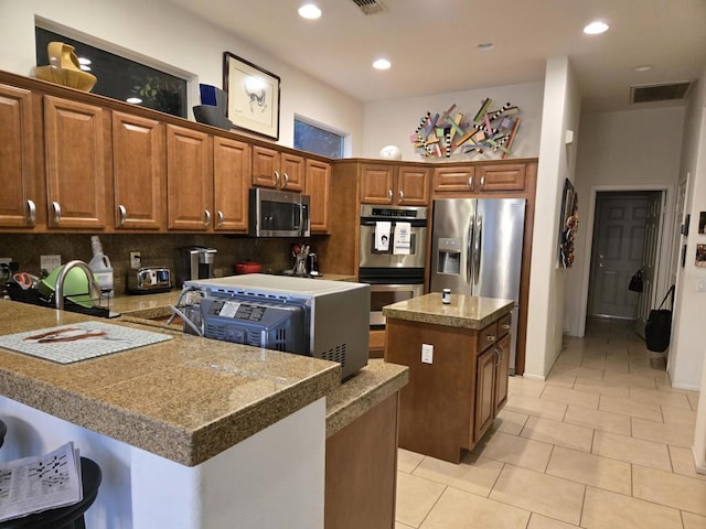 kitchen featuring stainless steel appliances, tasteful backsplash, a center island, and light tile patterned flooring