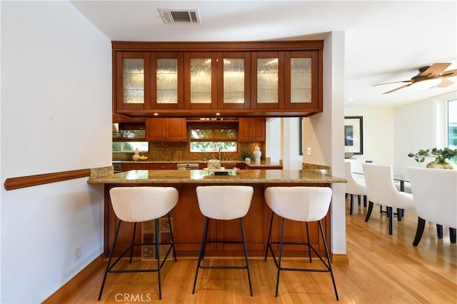 bar featuring stone countertops, sink, decorative backsplash, ceiling fan, and light hardwood / wood-style floors