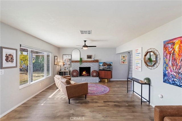 living room with dark hardwood / wood-style flooring, a brick fireplace, and ceiling fan