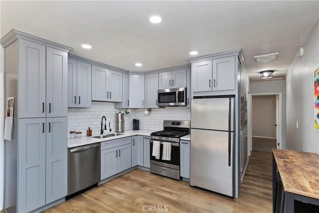 kitchen with sink, light hardwood / wood-style flooring, appliances with stainless steel finishes, gray cabinetry, and tasteful backsplash