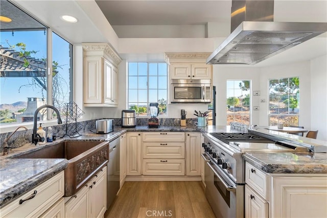 kitchen with dark stone countertops, cream cabinetry, stainless steel appliances, and island range hood