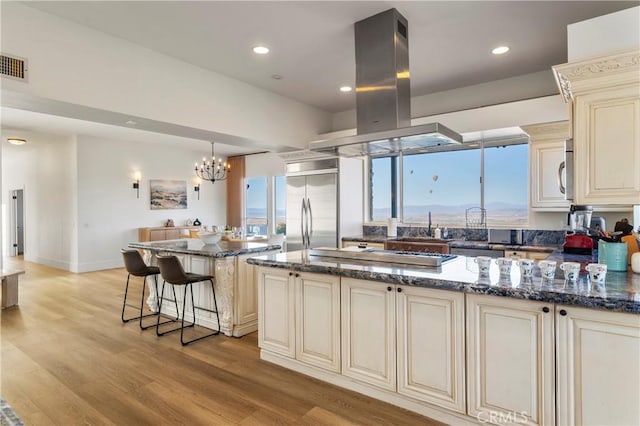 kitchen featuring appliances with stainless steel finishes, dark stone countertops, island range hood, a kitchen island, and cream cabinetry