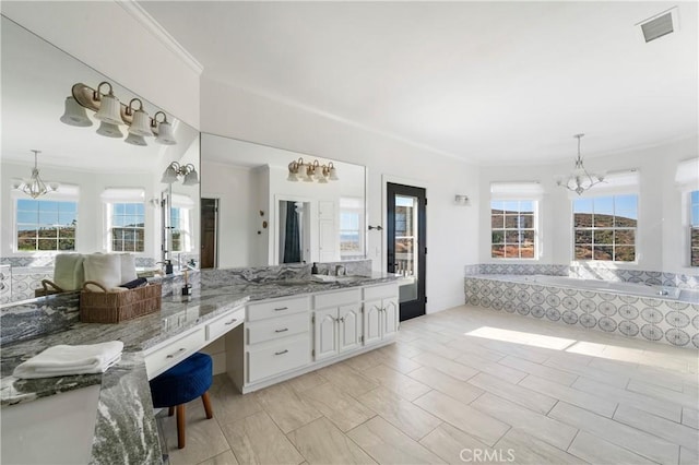 bathroom with an inviting chandelier, vanity, tiled bath, and a wealth of natural light