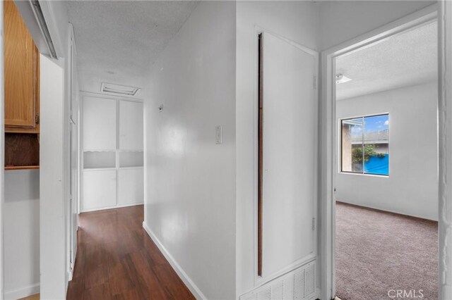 corridor with baseboards, visible vents, a textured ceiling, and dark wood-style floors