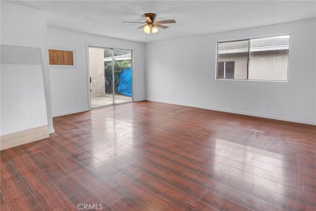 empty room with wood finished floors, a textured ceiling, a ceiling fan, and baseboards